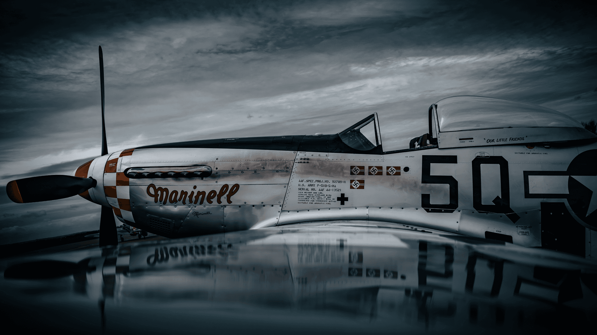 A vintage military fighter aircraft with 'Marinell' written on it, featuring a black and white checkered pattern, parked on a reflective surface under a cloudy sky.