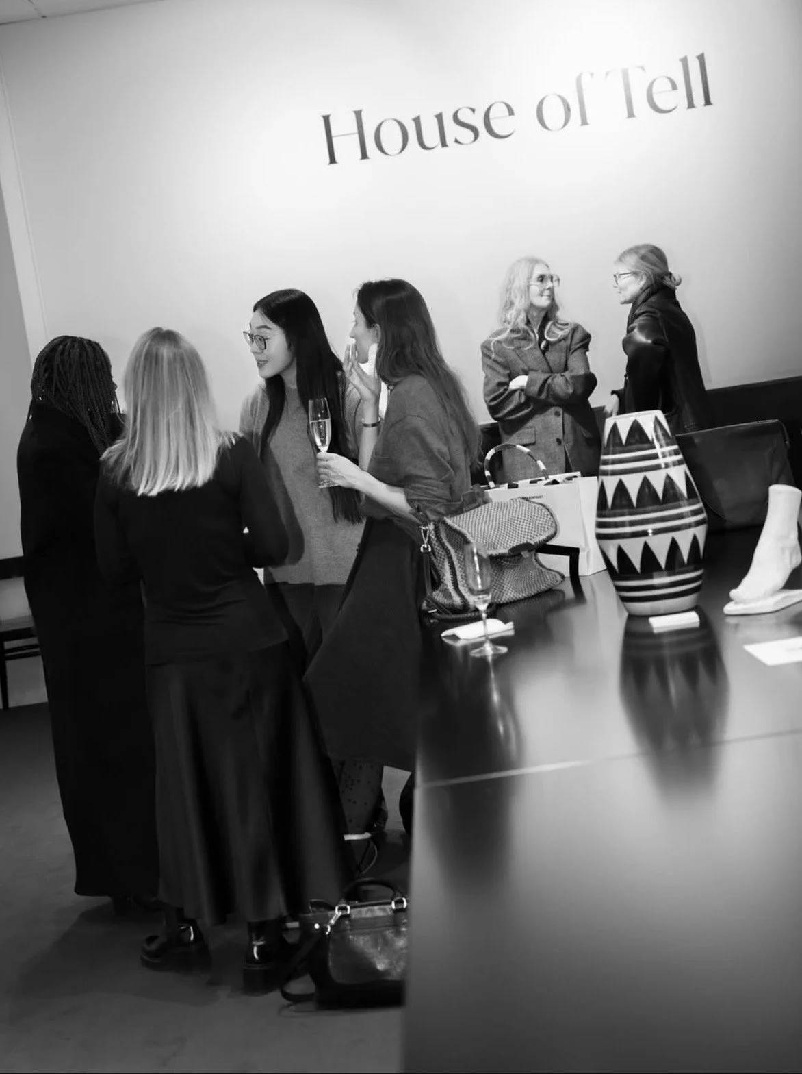 Group of women socializing at a gathering with a sign that reads 'House of Tell' on the wall