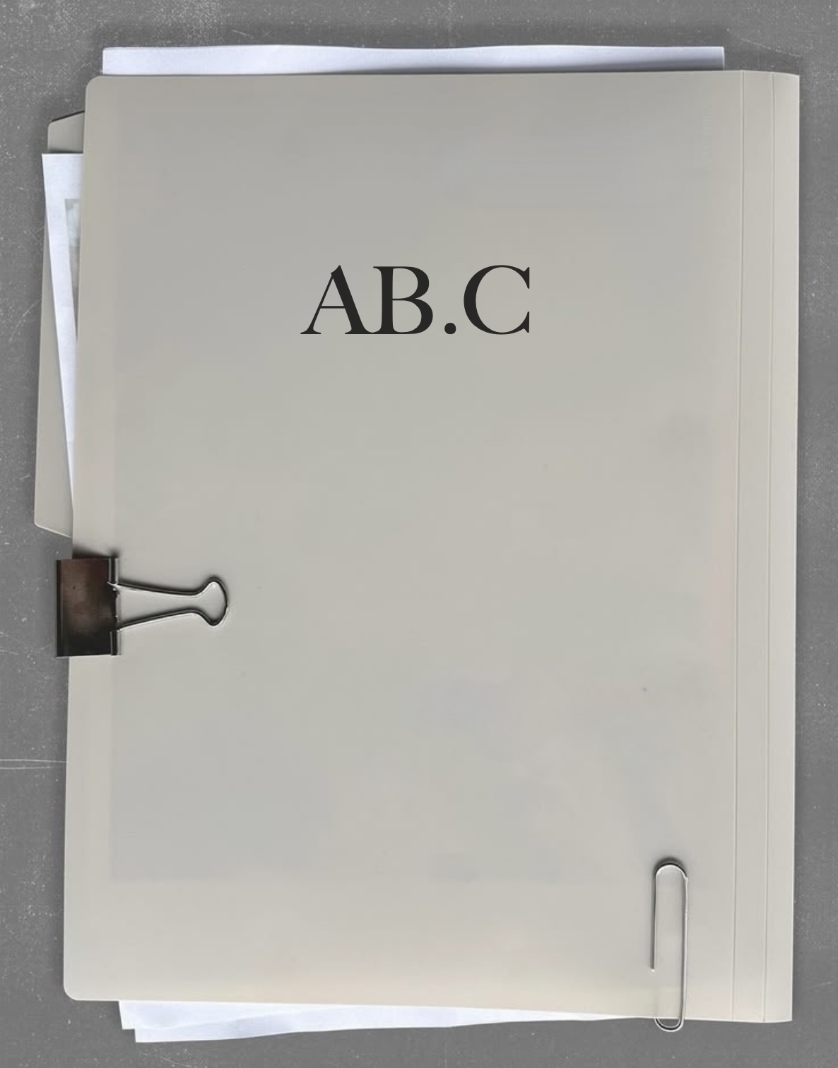 File folder labeled 'A B . C' with a metal binder clip and paper clip, placed on a gray surface.