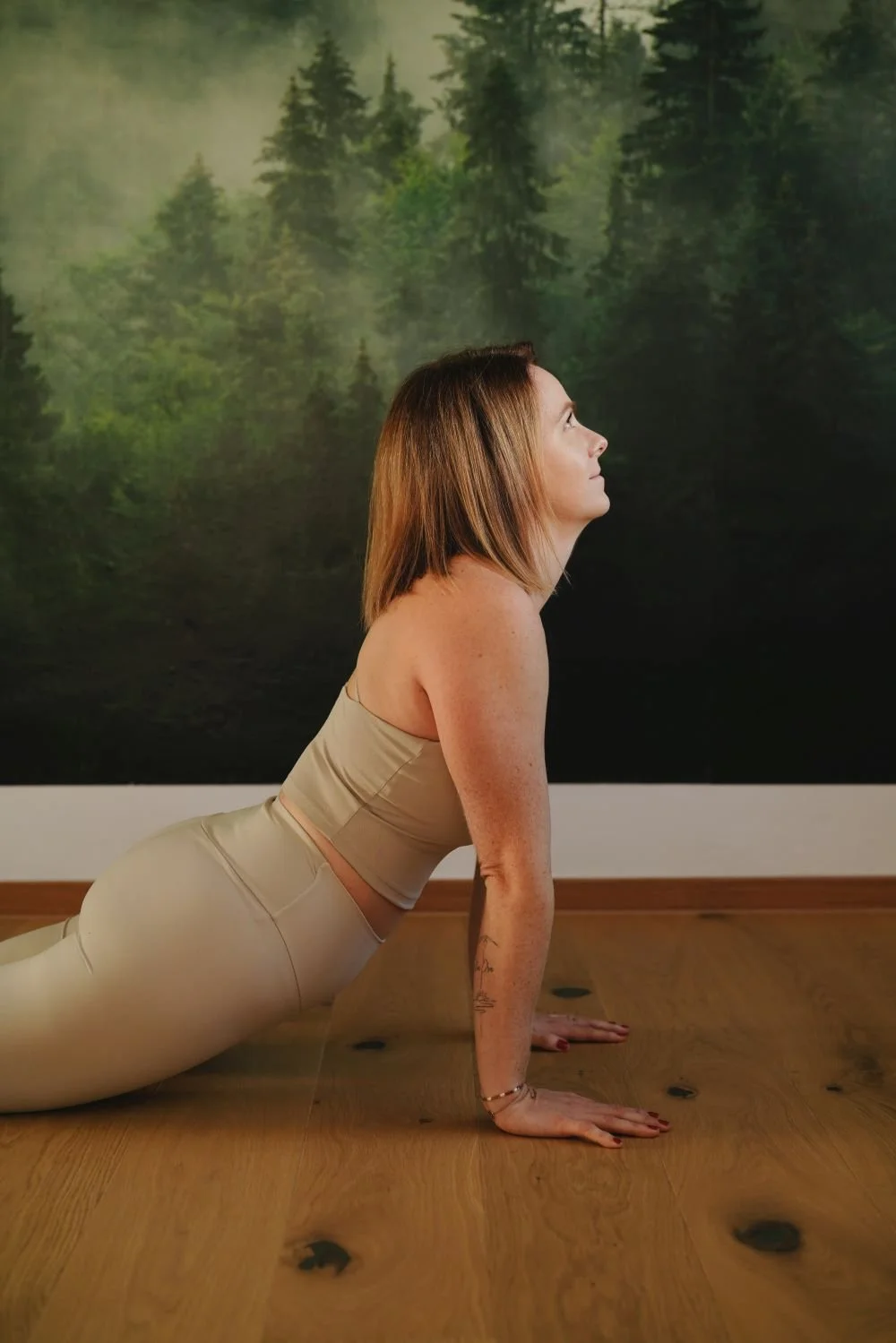 Frau in Yoga-Pose auf Holzfußboden vor einer Wand mit Waldmotiv