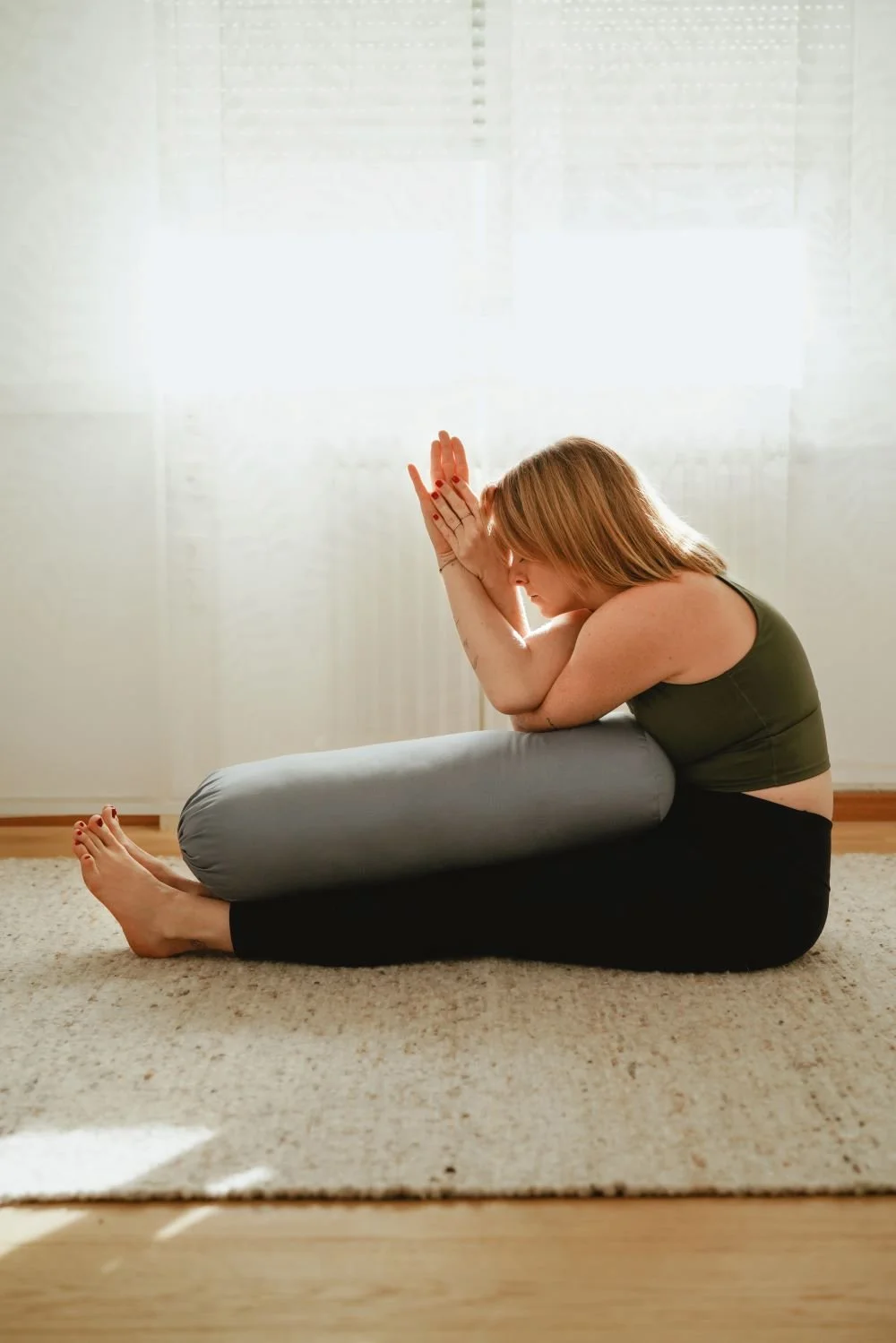 Eine Frau macht eine Yoga-Übung auf einem Teppich in einem Raum mit viel natürlichem Licht.