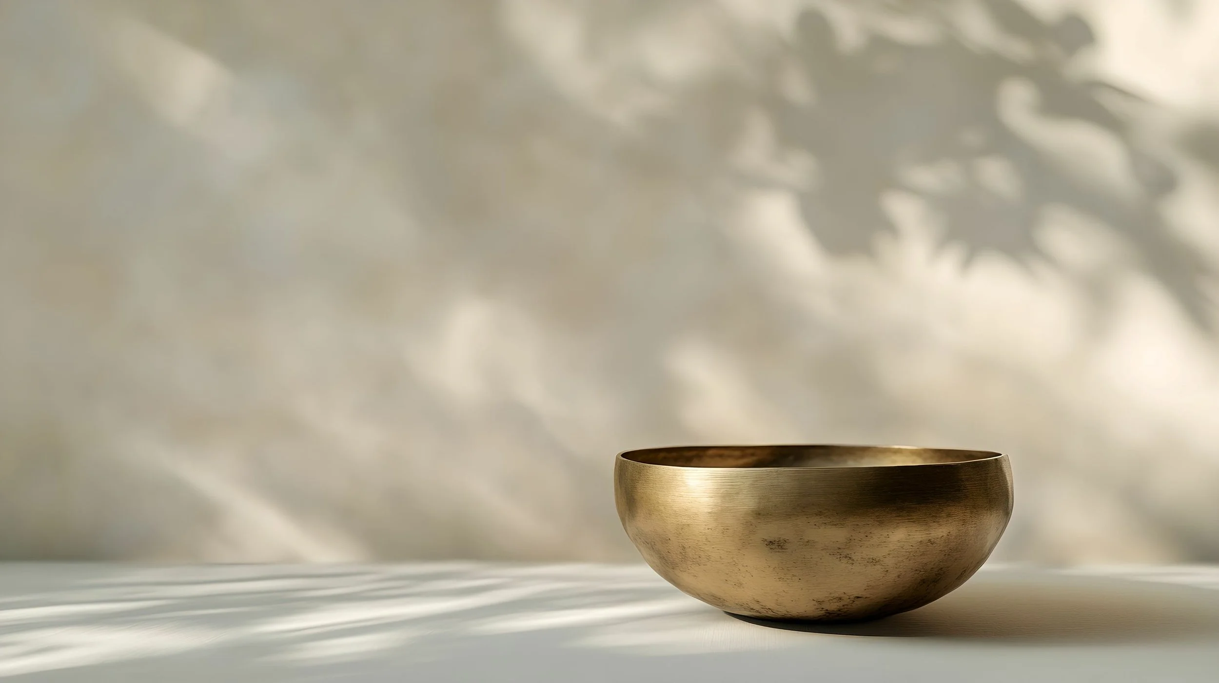 Eine goldene Schale auf einer weißen Oberfläche, Schatten an der Wand im Hintergrund.