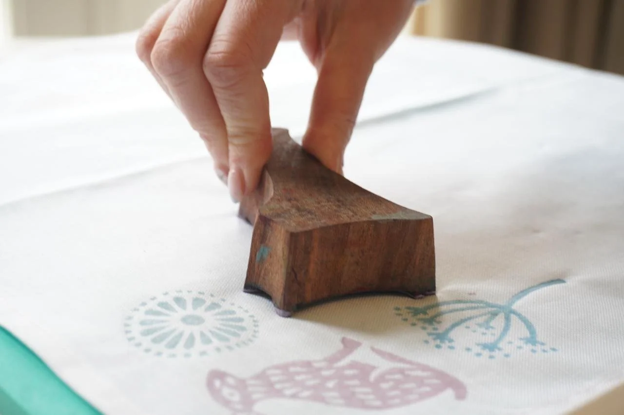 Close-up of a hand pressing a wooden stamp onto fabric with colorful decorative patterns.