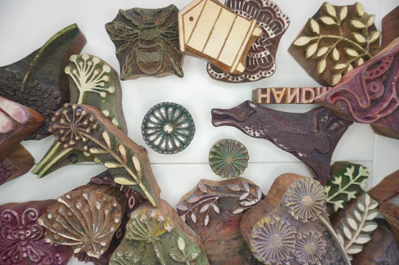 Collection of decorative wooden stamps and carved clay or ceramic buttons with nature-inspired and intricate patterns.