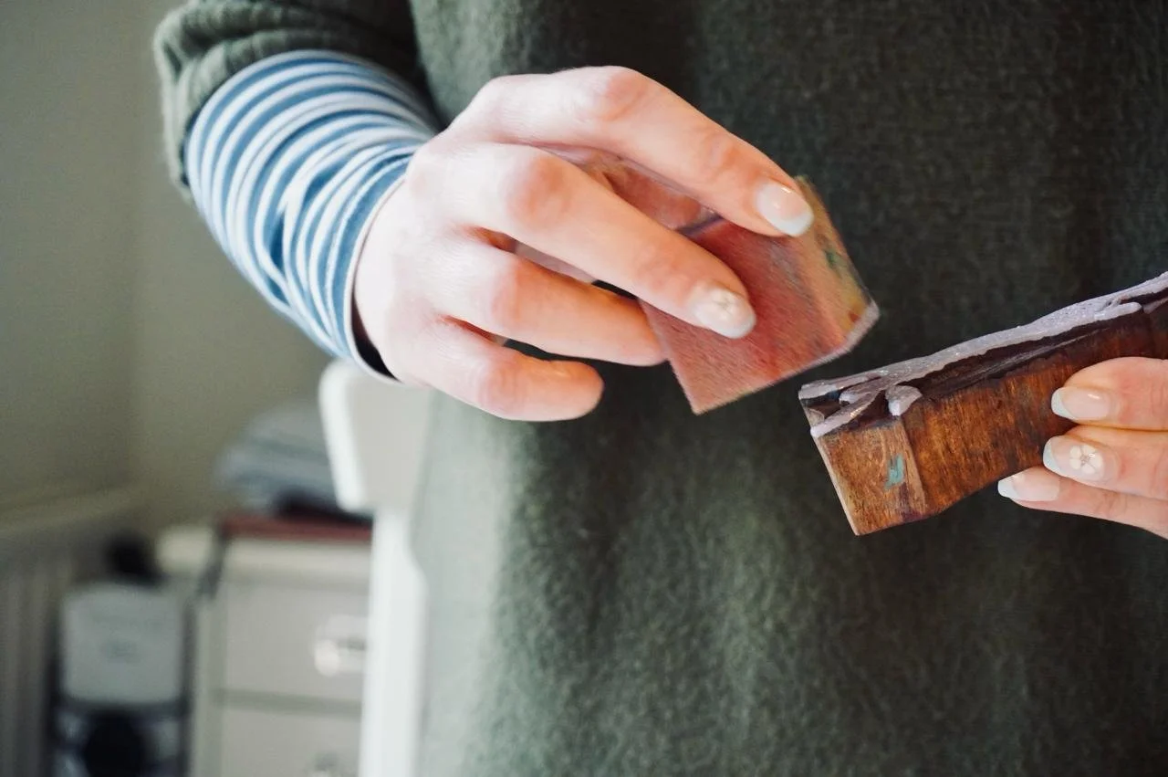 Person polishing a wooden object with a cloth, wearing a striped shirt.