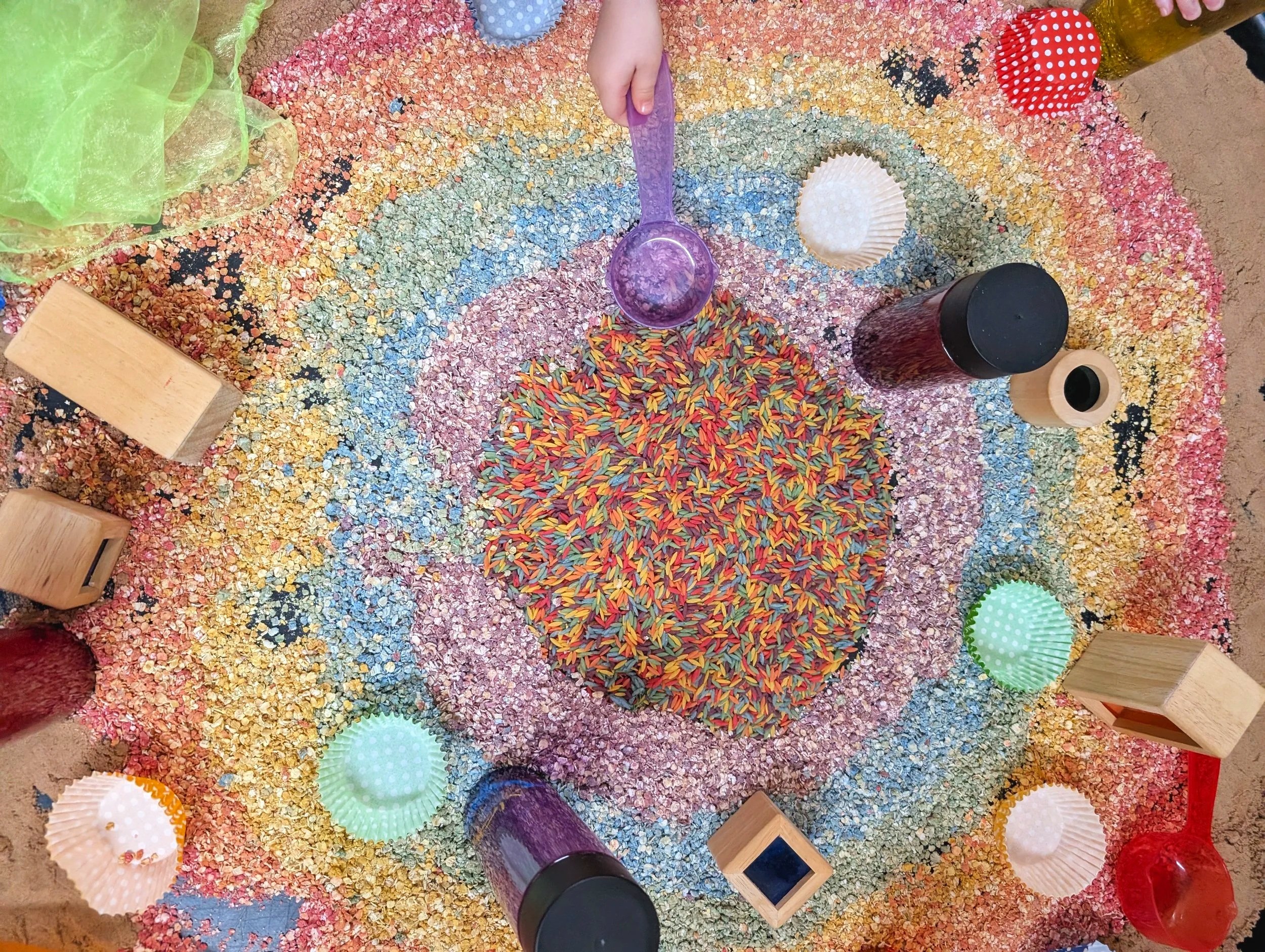 Colorful sand art display with rainbow design, cupcakes, jars of sand, and green paper cupcakes.