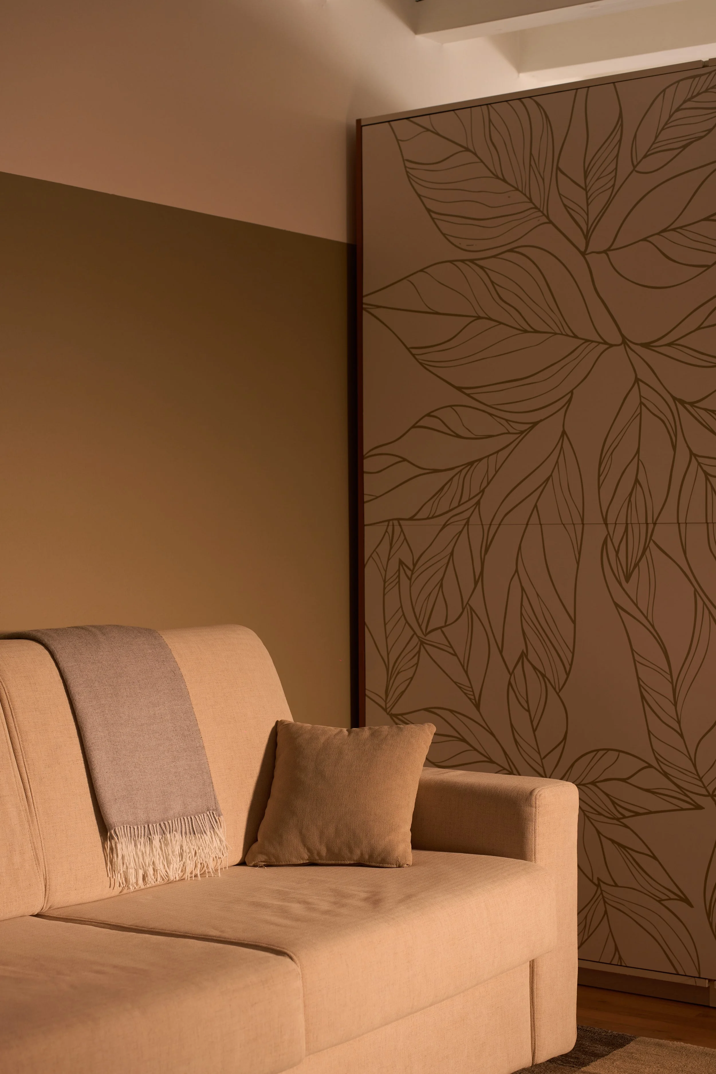 Un divano beige con un cuscino e una coperta, a fianco un armadio con decorazioni.