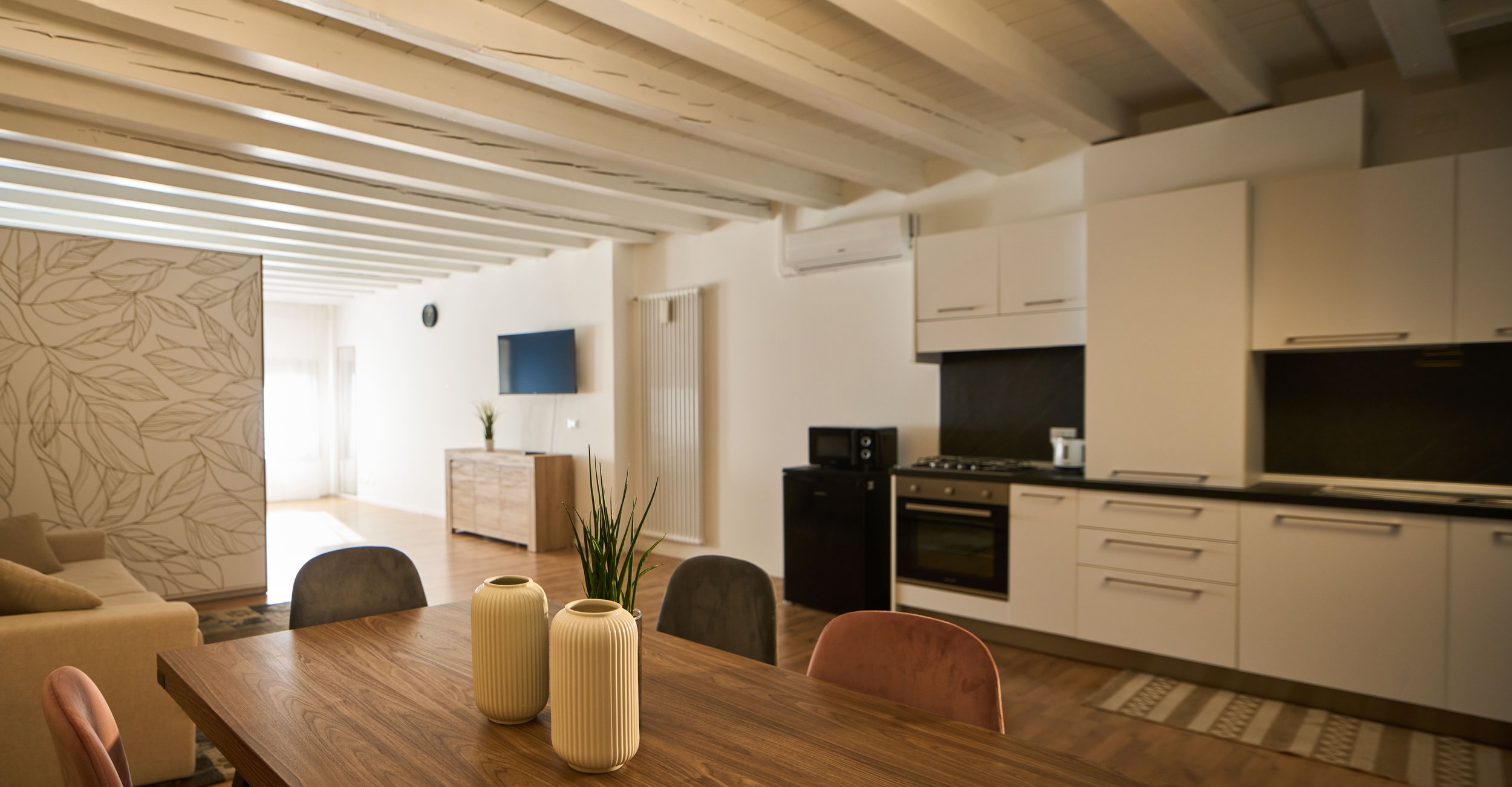 Appartamento moderno con cucina, tavolo in legno e vasi decorativi, rivestimento decorativo con foglie della parete armadio, soggiorno e zona TV.