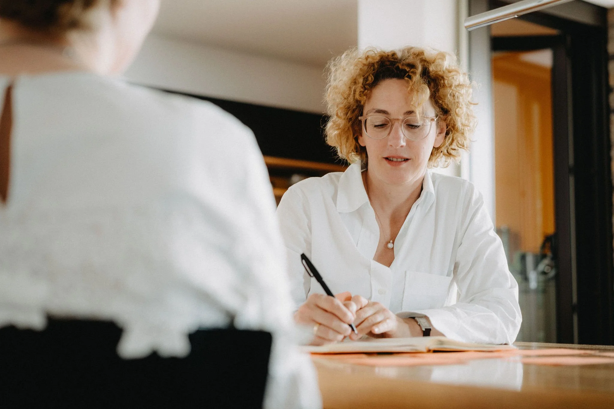 Ina Vössing in einer Coaching Situation am Tisch. Sie macht sich Notizen, die Klientin sitzt ihr gegenüber.