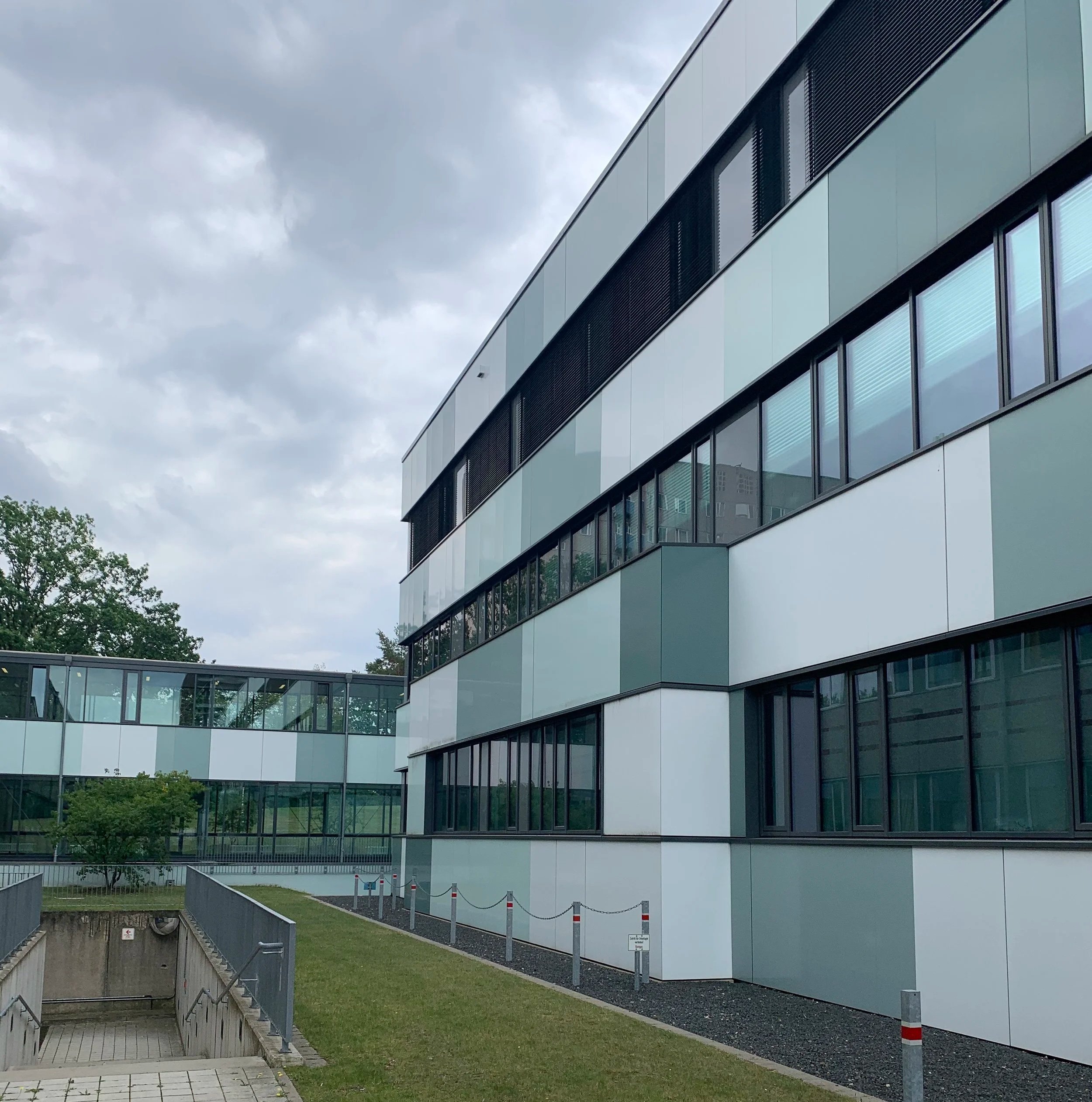 Die Fassade eines Gebäudes mit grünlichen und weißen Fassadenplatten und durchlaufenden Fensterbändern.