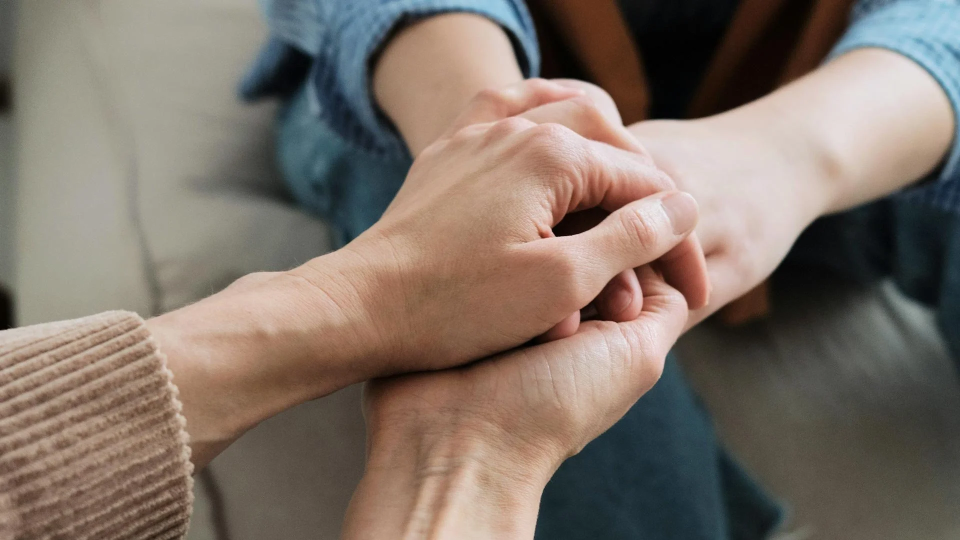 Two people holding hands, one person gently grasping the other's wrist, indicating a comforting gesture.
