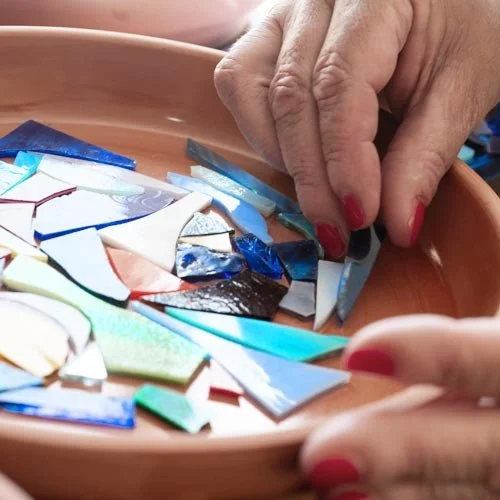 Close-up of a person arranging colorful broken glass pieces on a tray.