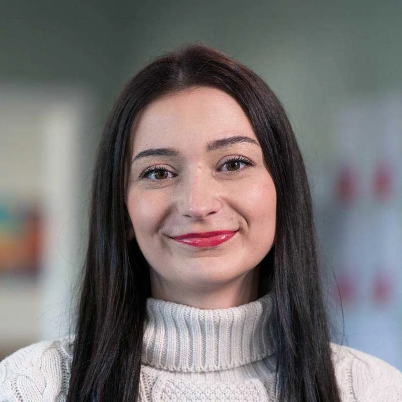 A woman with long dark hair wearing a cream turtleneck sweater smiling at the camera.