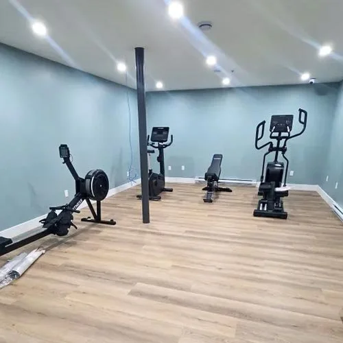 Private, personalized care at Vida Nova Recovery Centre. Gym with exercise machines, including an elliptical trainer, a rowing machine, a stationary bike, and an elliptical trainer, in a room with wood flooring and blue walls.