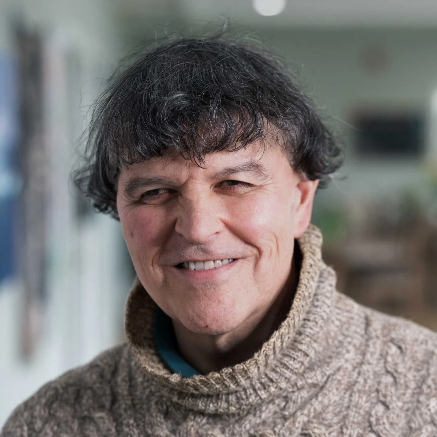 A smiling man with dark hair wearing a beige sweater.