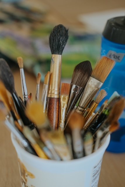 Paintbrushes in a white container, with a blue paint tube and blurred background.