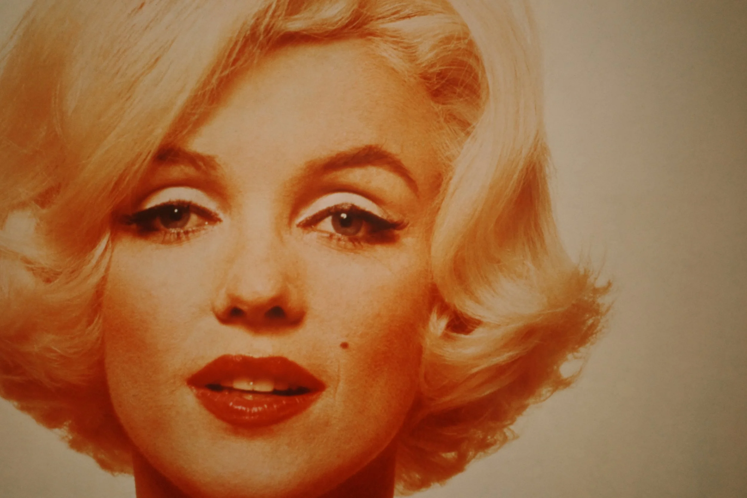 Close-up of a vintage poster or painting of a woman with blonde hair, red lipstick, and makeup, possibly from the 1950s.