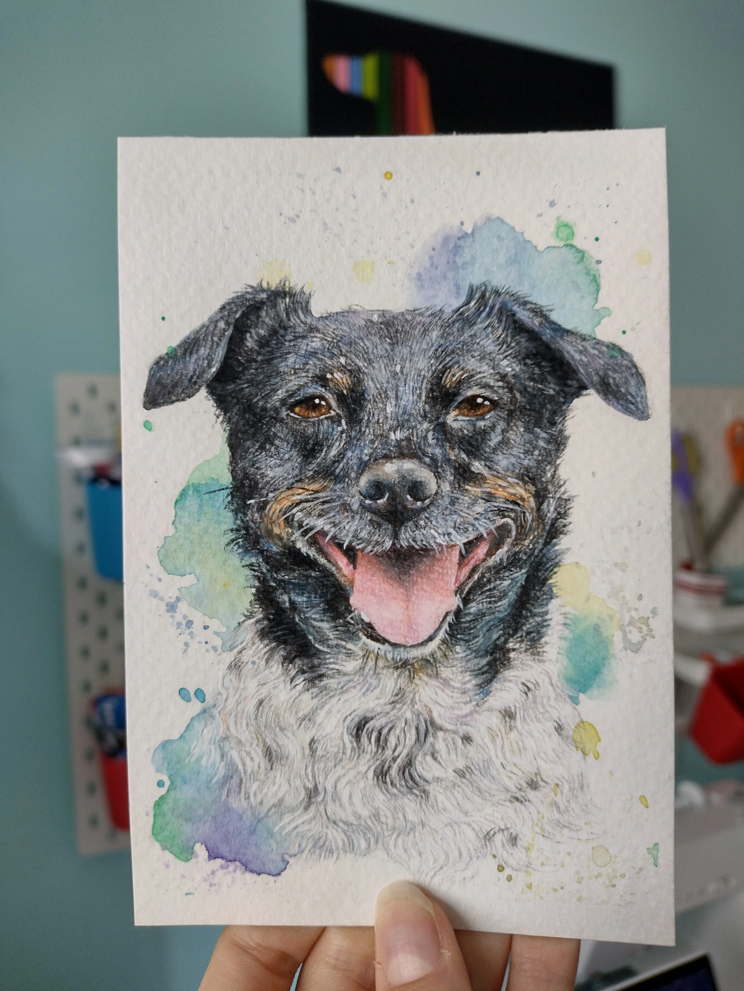 Watercolor painting of a happy black and tan dog with a pink tongue, surrounded by colorful splashes of watercolor.