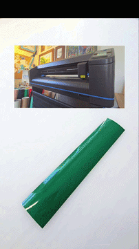 A large format printer printing on a green roll of material, with the printed area visible in the photo.