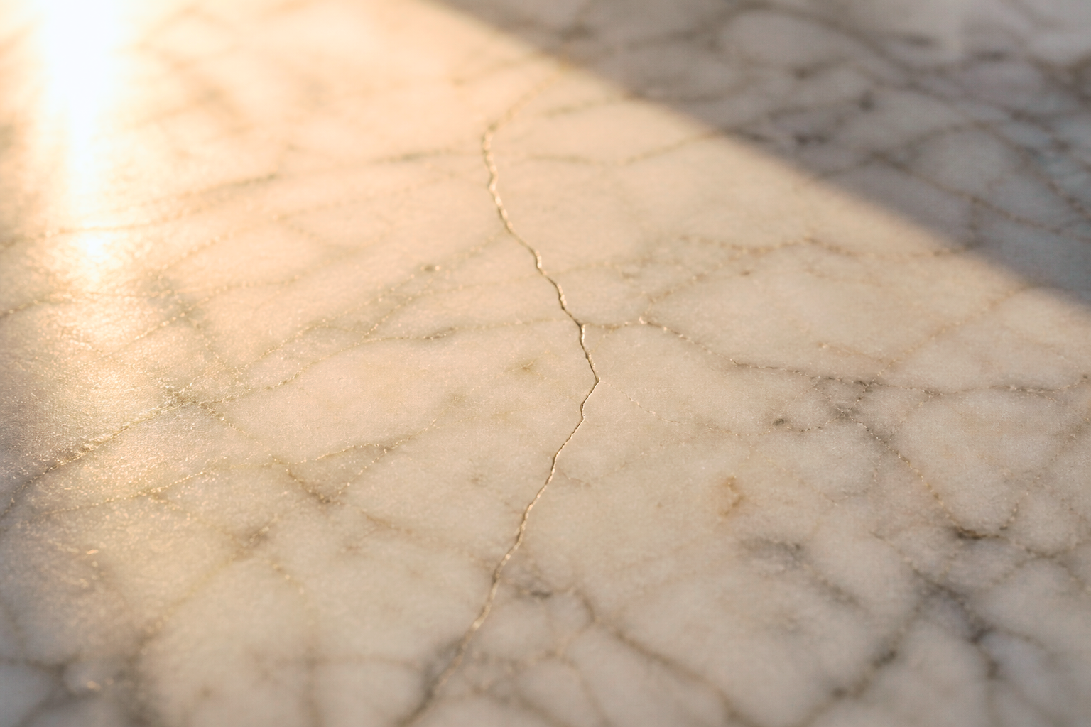 Close-up of a cracked, beige marble surface with a subtle pattern and warm lighting.