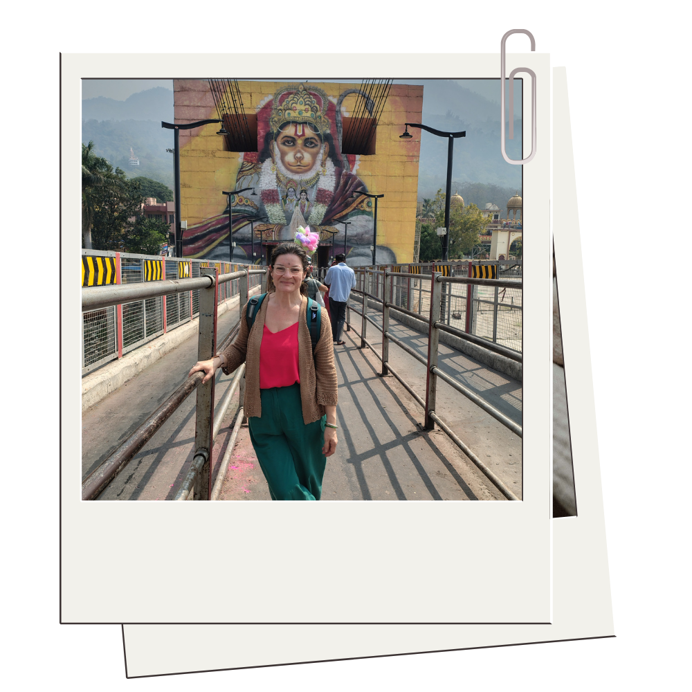 Woman smiling on a bridge with a large mural of Hanuman in the background.