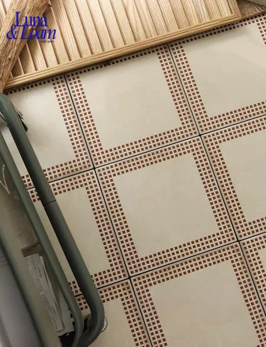 Close-up of a tiled floor with a beige and red mosaic pattern, part of a wooden kitchen tray, and a metal cart leg.