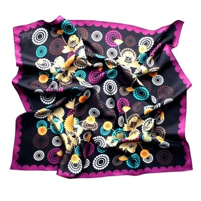 Colorful fabric with a black background, adorned with various circular patterns and stylized lizard or gecko designs in multiple colors, bordered with a pink scalloped edge.