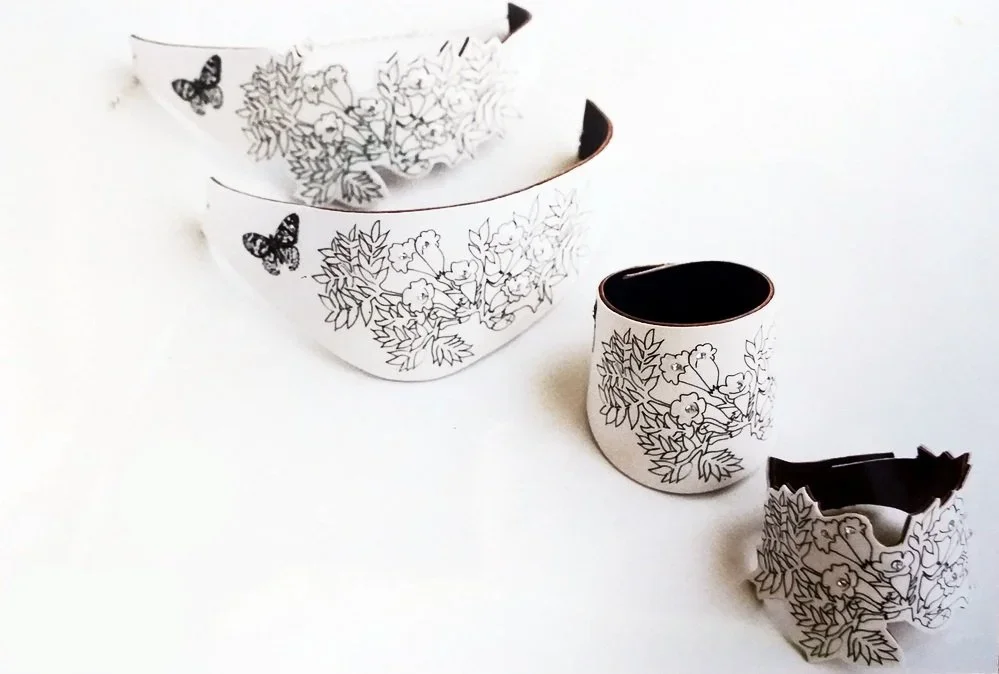 Four white paper rings with black floral and butterfly designs, arranged in a diagonal line on a white surface, with the smallest at the front and the largest at the back.