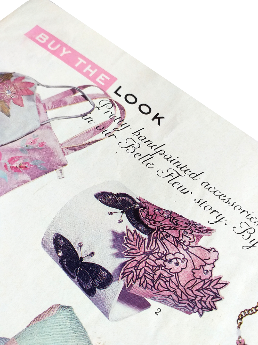 Close-up of a magazine page with a pink floral handbag, butterflies, and promotional text about buying handpainted accessories from Belle Fleur story.