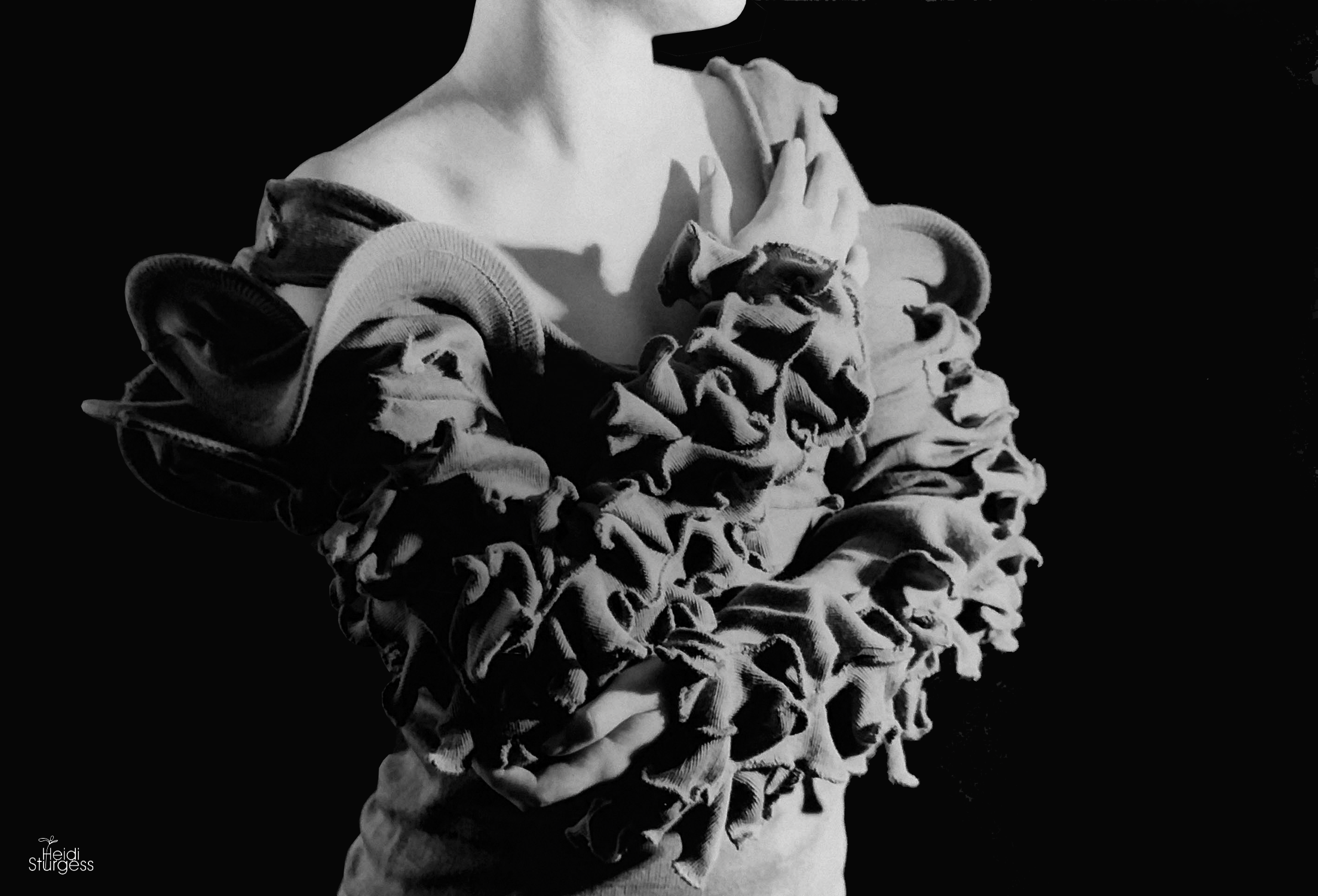 Black and white photo of a person with crossed arms, wearing a loose off-shoulder top and ruffled pants.