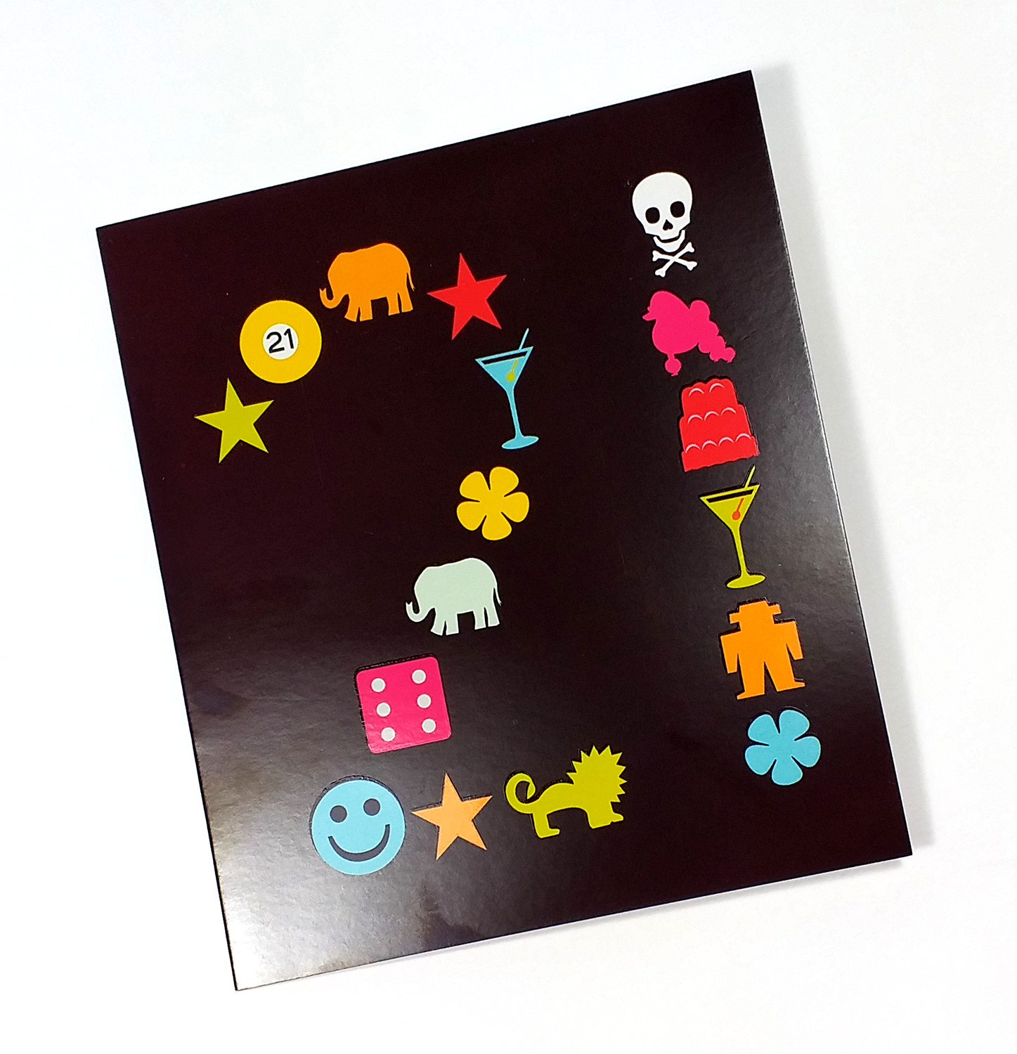 A black sheet with colorful emojis and symbols, including an elephant, a peace symbol, a pinball ball with the number 21, stars, a cocktail glass, a pink poodle, a red layered cake, a skull and crossbones, a smiling face, a yellow lion, a six-sided d