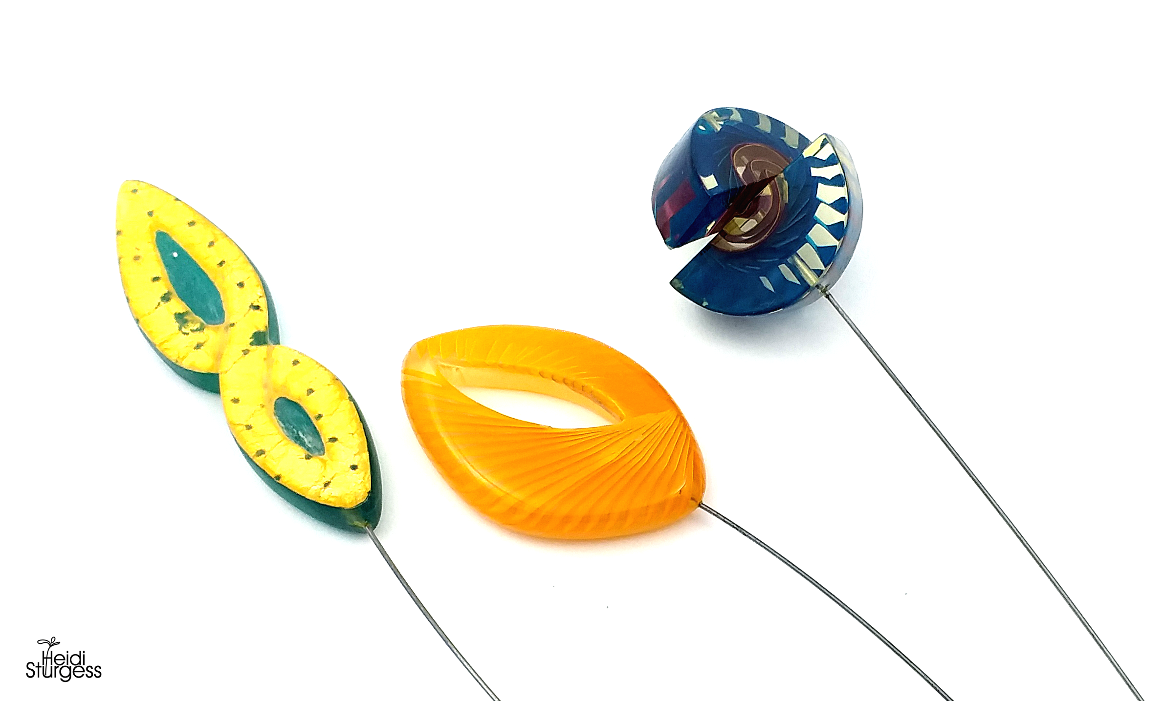 Colorful glass art sculptures resembling abstract leaves and shells are shown on thin metal rods against a white background.