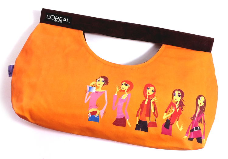 Orange fabric clutch purse with illustrated women on the front, and a black trim band labeled 'L'ORÉAL PARIS' at the top.