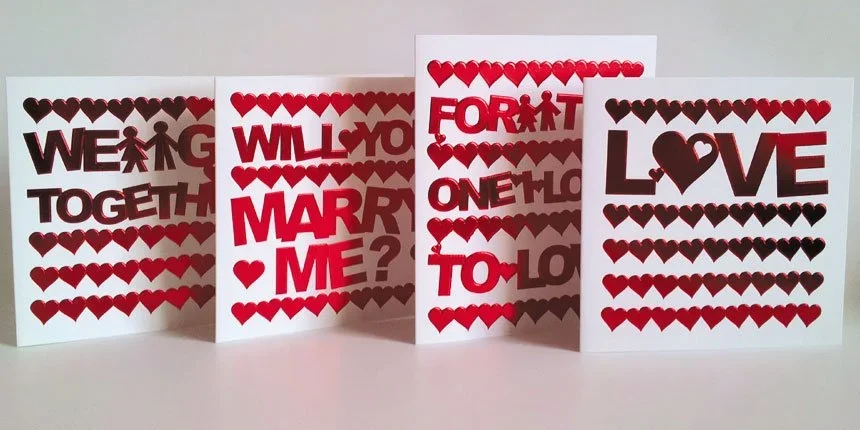Four greeting cards with heart patterns and romantic messages, including 'WEDDING TOGETHER,' 'WILL YOU MARRY ME?,' 'FORGET ONE LOVE,' and 'LOVE,' displayed on a white surface.
