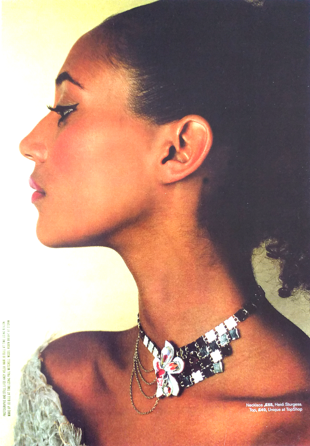 Profile of a woman with dark hair styled back, wearing a layered necklace with a butterfly pendant and a textured off-shoulder top.