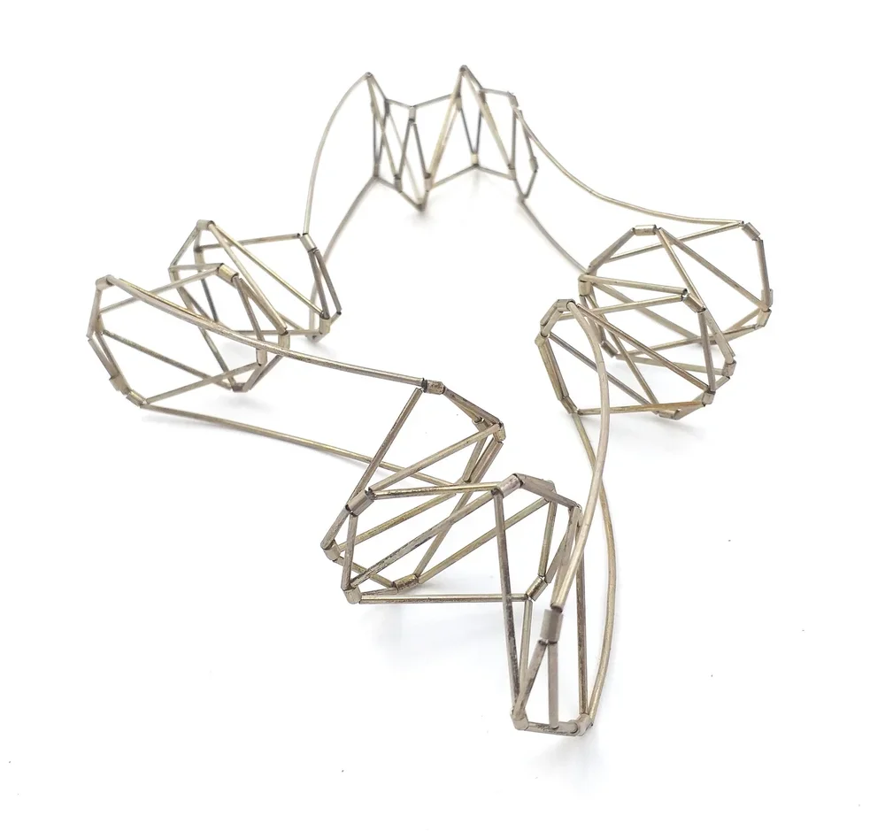 A jewelry piece made of metal, shaped like an angel or fairy with wings and a halo, in a minimalist wireframe design.