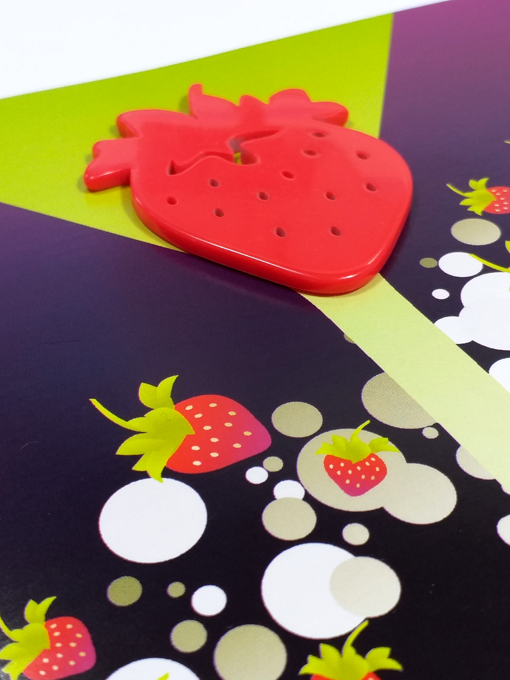 Close-up of a red silicone strawberry-shaped timer on a colorful tablecloth with strawberries and polka dot patterns.