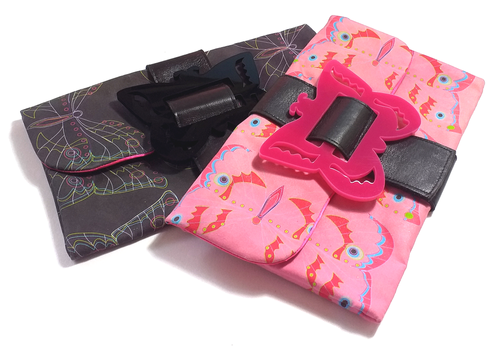 Two folded fabric pouches, one with a black background and colorful floral pattern, and the other pink with cartoon unicorns, with plastic quick-release buckle accessories on top.