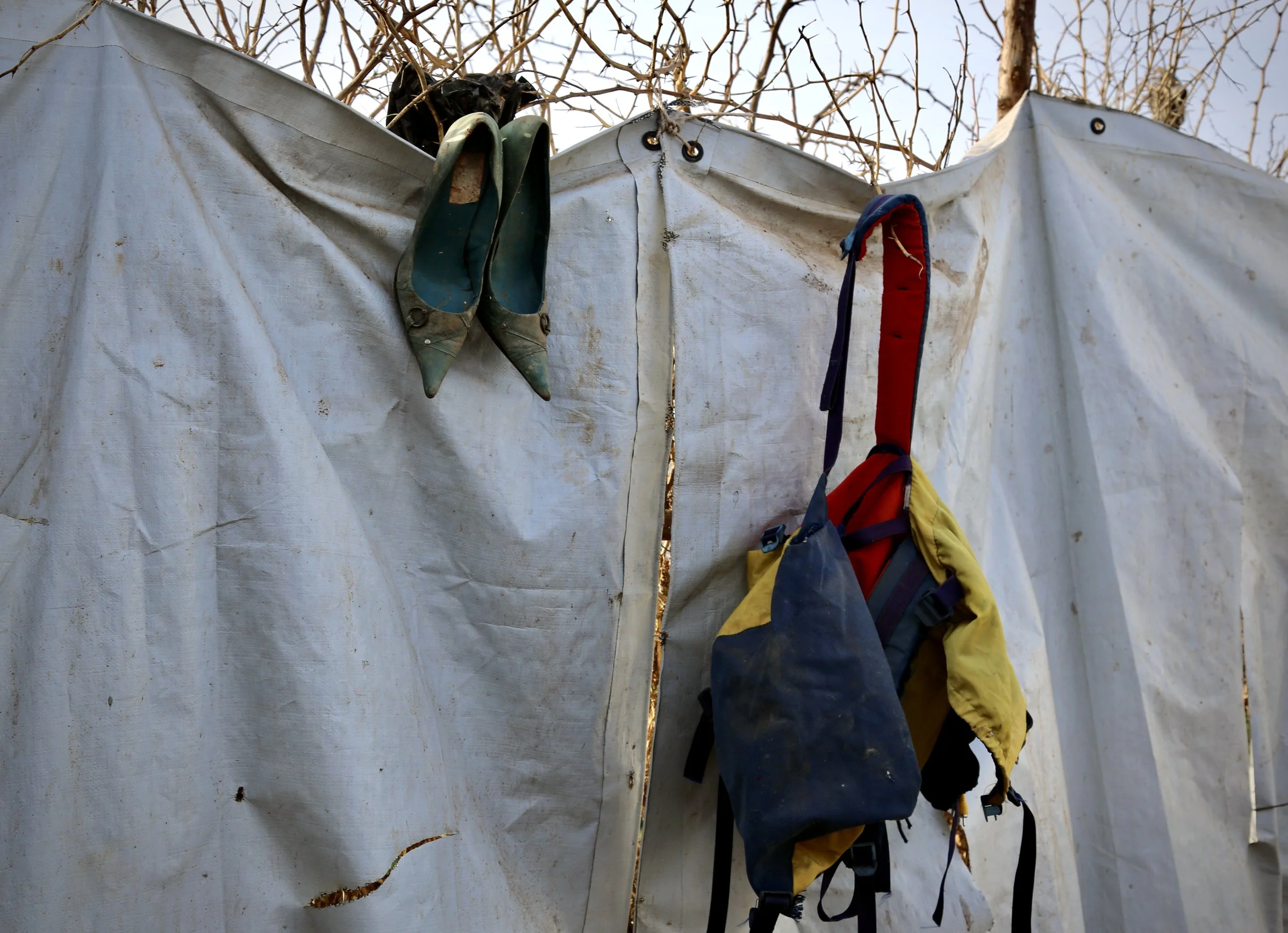Mud-stained high heels hang from a plastic sheet wall surrounding part of the settlement in Kakuma refugee camp.