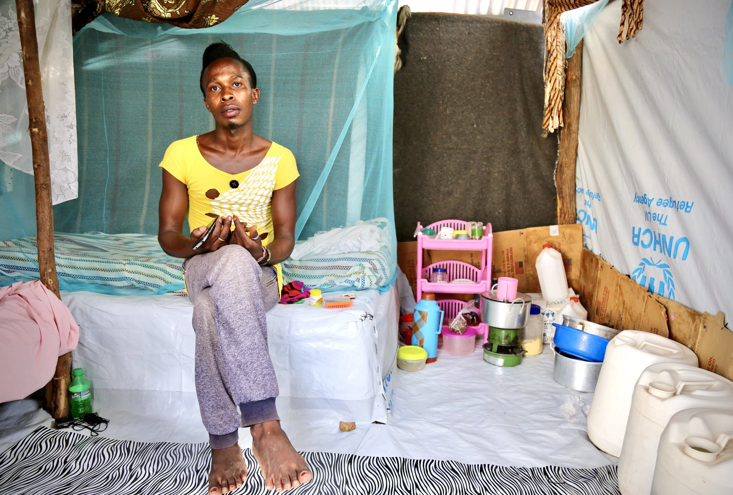 Charles Itwara sits inside her shelter in Kakuma refugee camp, where she lives among improvised walls, mosquito nets and household items assembled over years of displacement.
