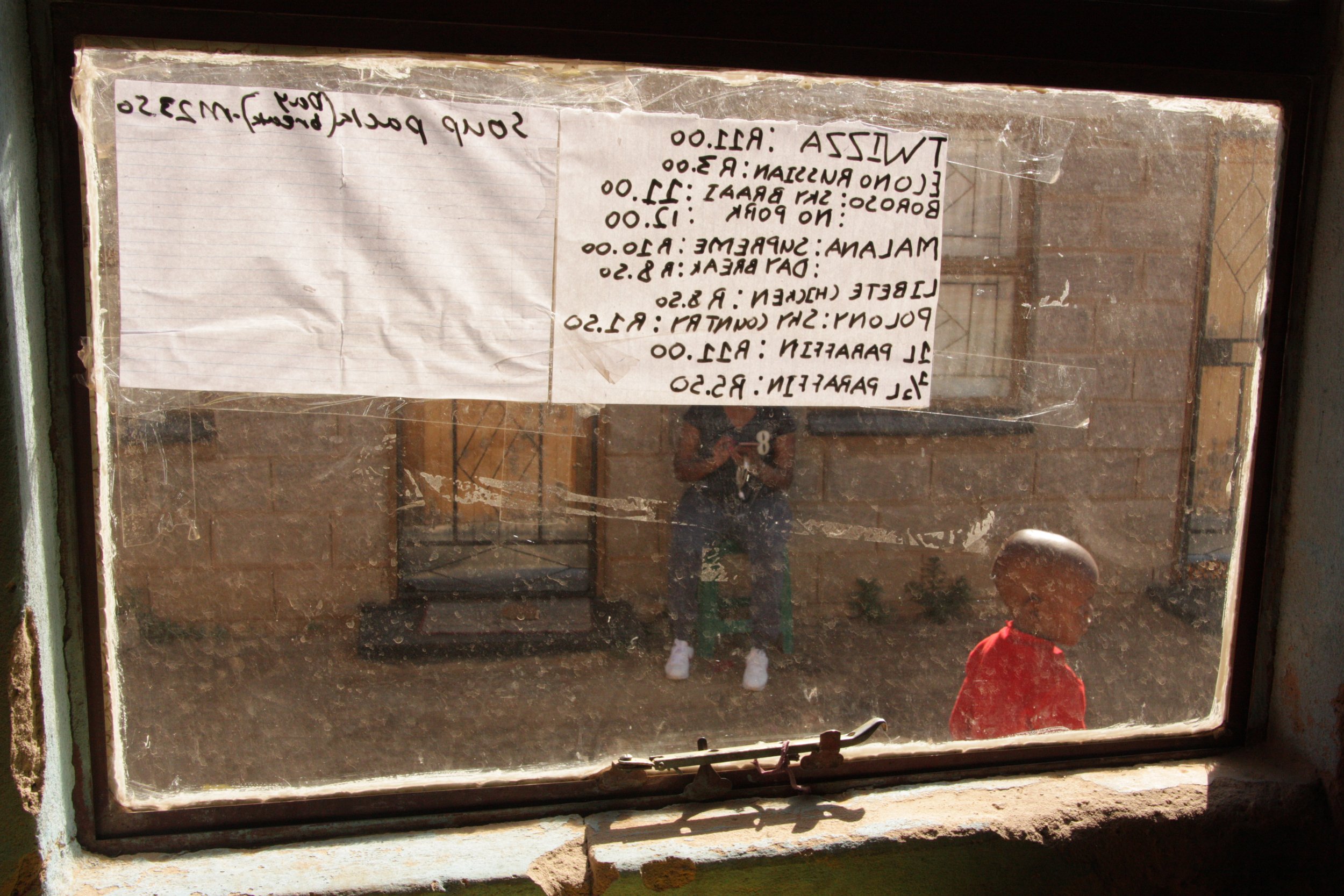 A child passes outside Paballo’s shop after school in Ha Magele, Leribe District, Lesotho. The storefront acts as both a small business and a gathering point within the neighbourhood, where children stop for snacks and residents meet throughout the d
