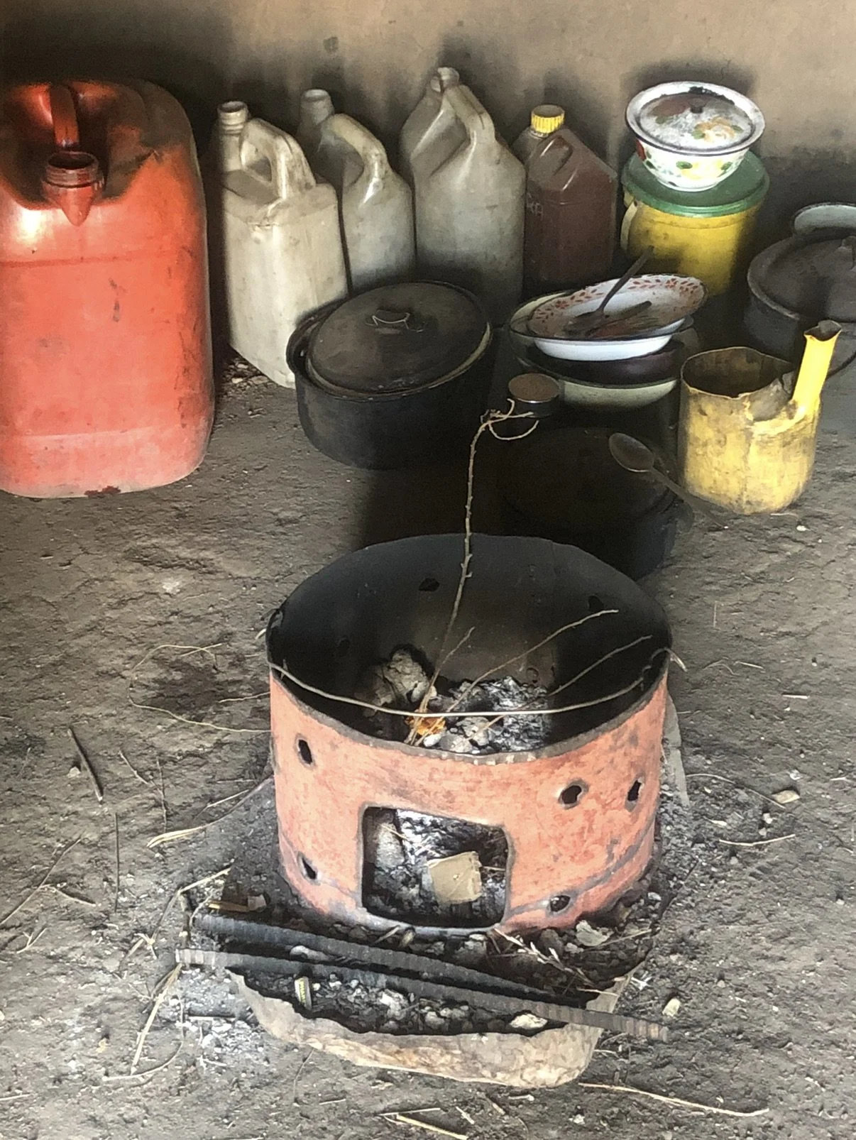A coal stove and cooking utensils inside the hut shared by Bokang Khera and his elderly caregiver. The single-room dwelling served as their kitchen, sleeping area with a shared blanket on the floor, and living space.