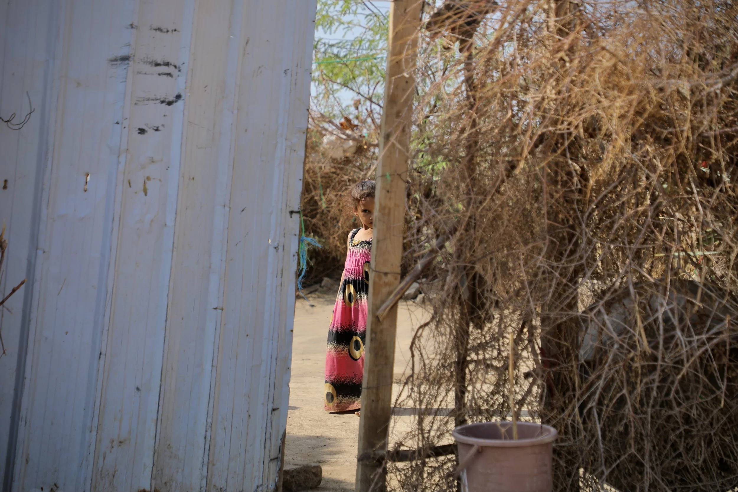 A child, Amar's daughter, stands at the entrance of the family home. Daily life resumes cautiously in areas once contaminated.
