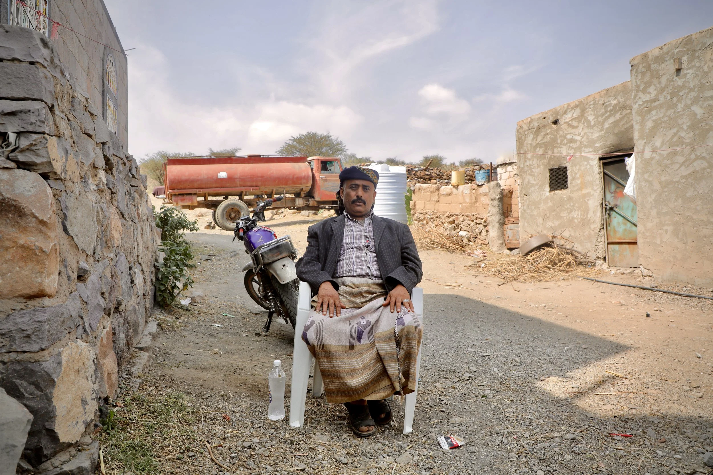 Saleh Abdullah Qassem, local chieftain, seated outside his home in Qatabah, Al Dhale Governorate. Demining teams subsequently discovered dozens of landmines in the precise location where he sits. The red tanker in the background is a marker of workin