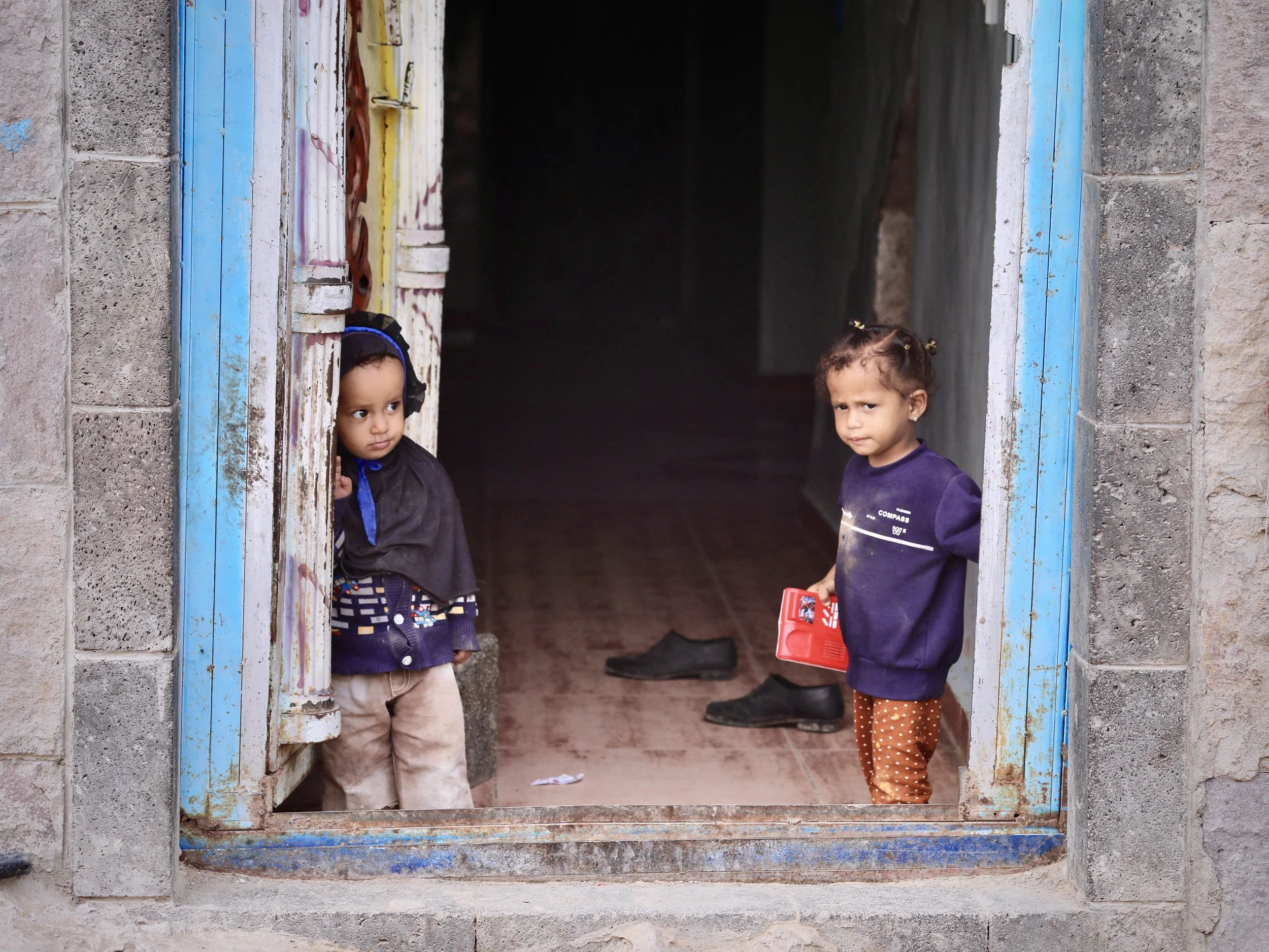 Grandchildren at the threshold of Mosaid Mohammed Ali Naji's home in Shakhab, Al Dhale. The families in this area returned from displacement to find their land and courtyards still contaminated with landmines and IEDs.