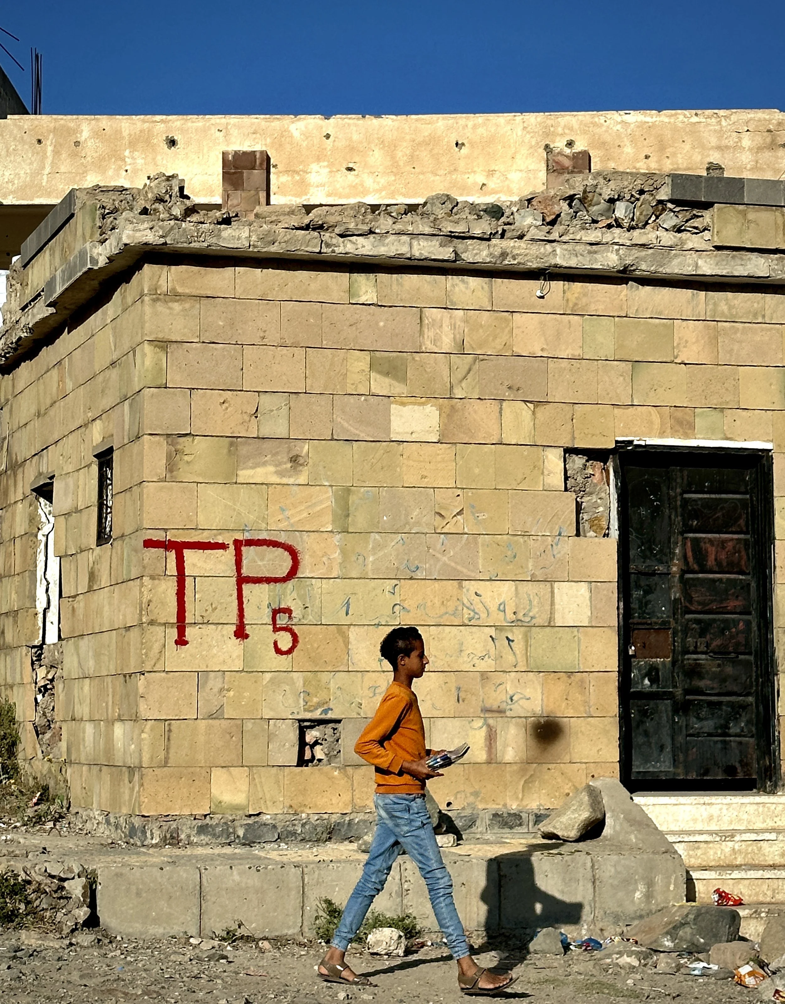 A child walks past a wall marked “TP5” inside Ibrahim Aqeel School in Taiz, Yemen. In humanitarian mine action, “TP” refers to a “Turning Point,” a surveyed marker used to indicate a change in the boundary of a suspected or confirmed hazardous area d