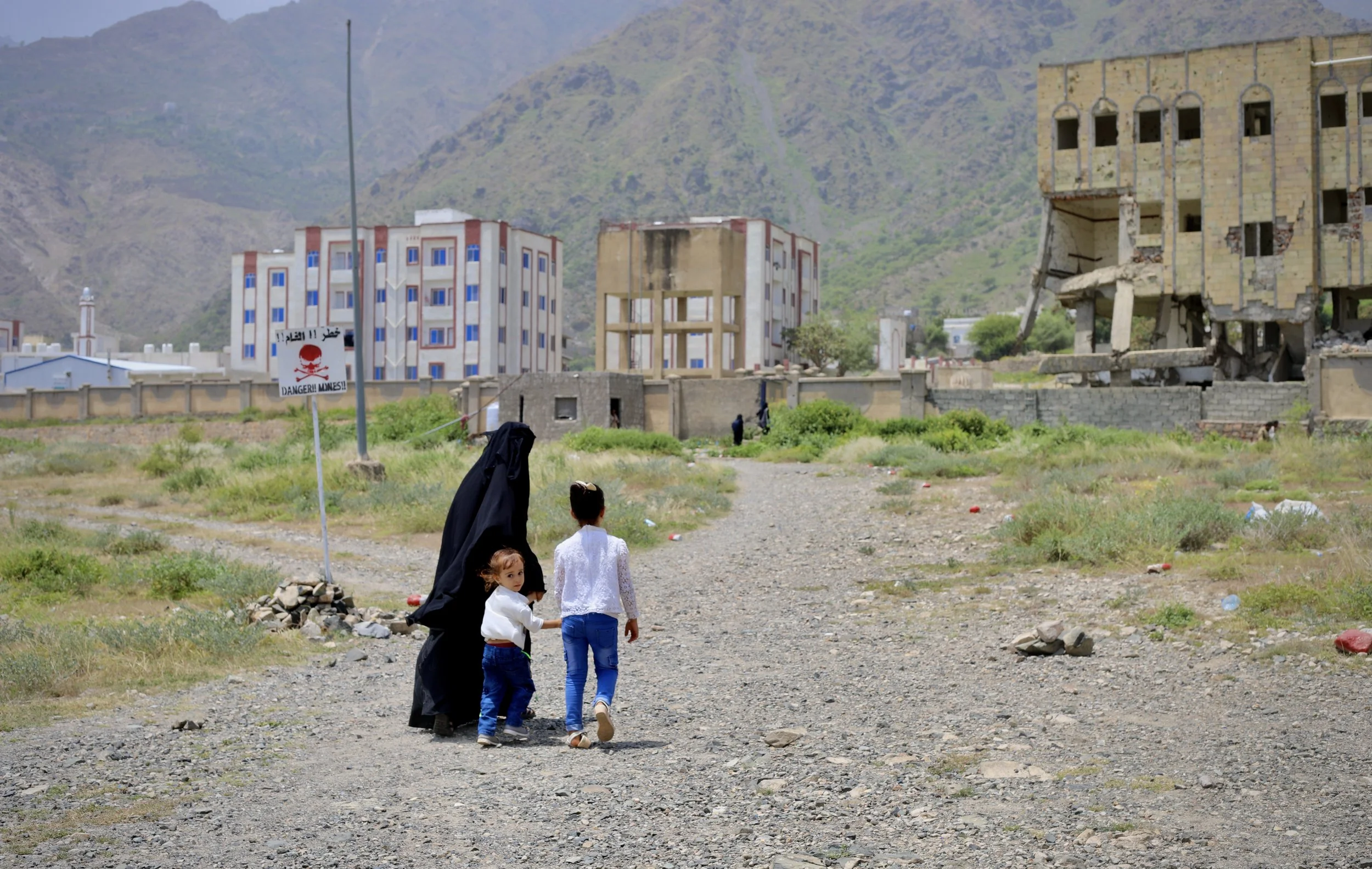 A woman and her children walk toward Ibrahim Aqeel School in Taiz, where students continue attending classes despite extensive war damage to the campus and the continuous presence of landmines in the vicinity.