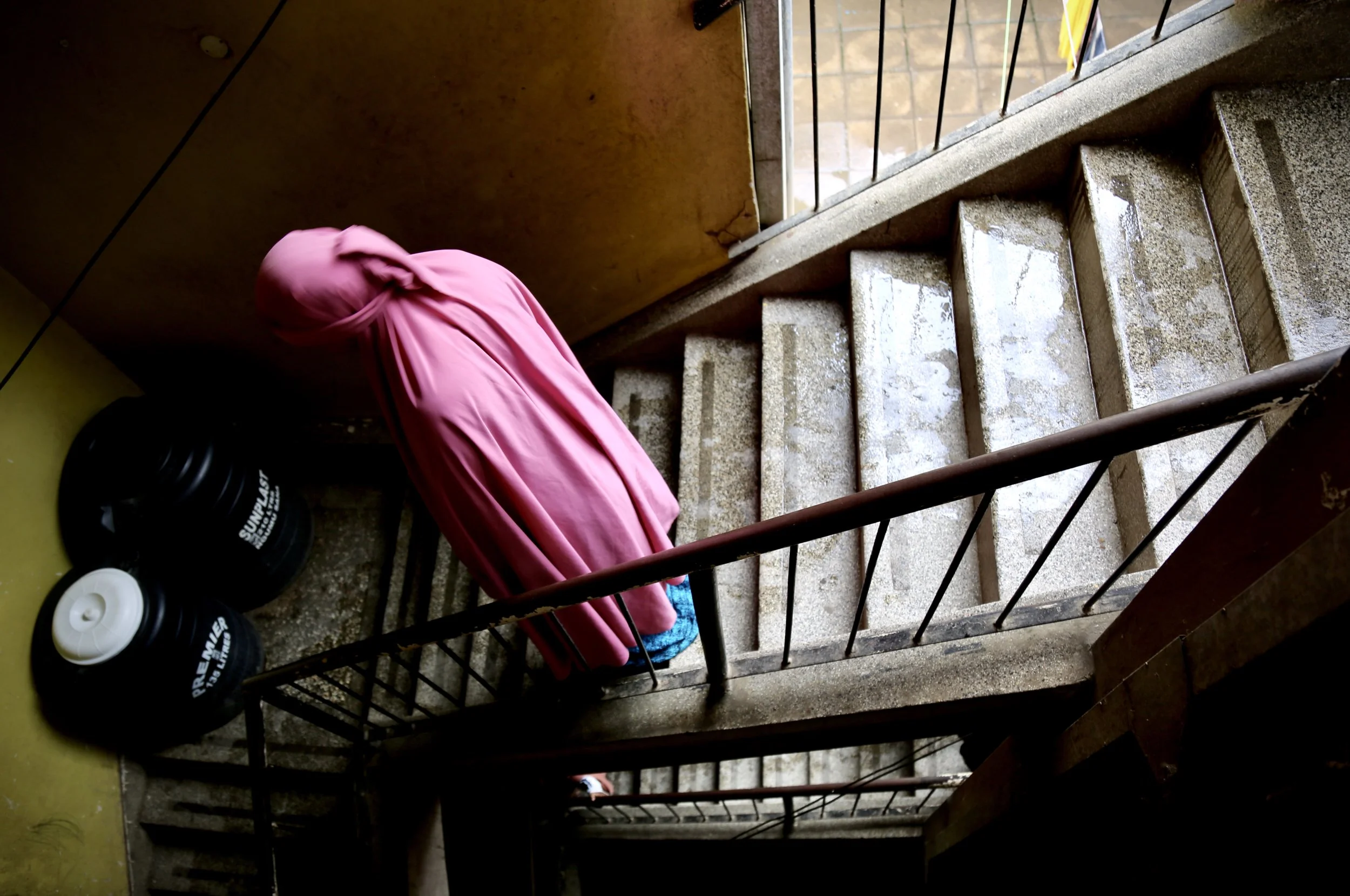 A young Somali refugee woman descends a staircase in an apartment block in Eastleigh, Nairobi. The sisters often used side streets and avoided unnecessary travel because of fears of police checks and arrest. Nairobi, Kenya, June 2016.