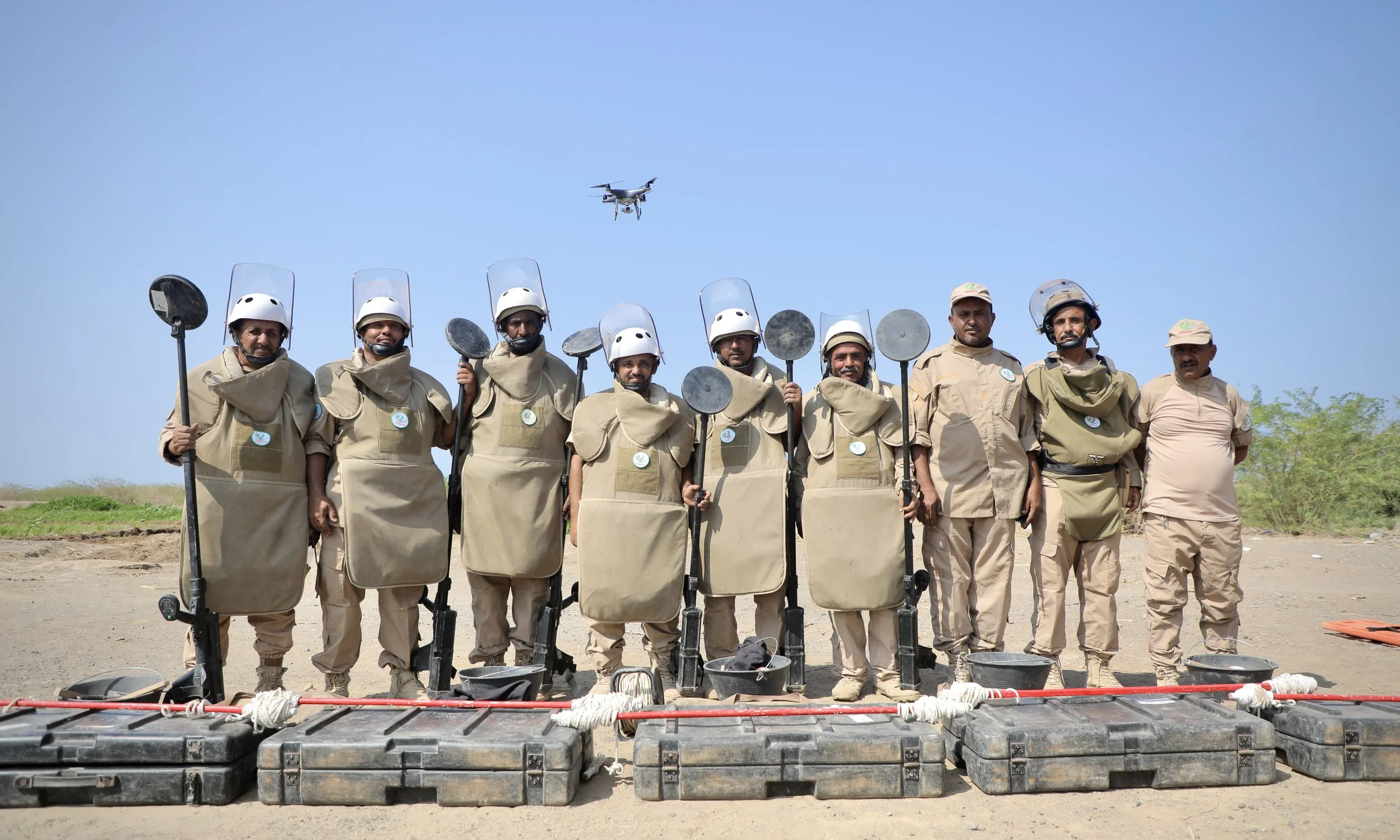 Members of Team 21 pose with their equipment in Al Remah below a drone, near Mocha, Taiz governorate, Yemen.