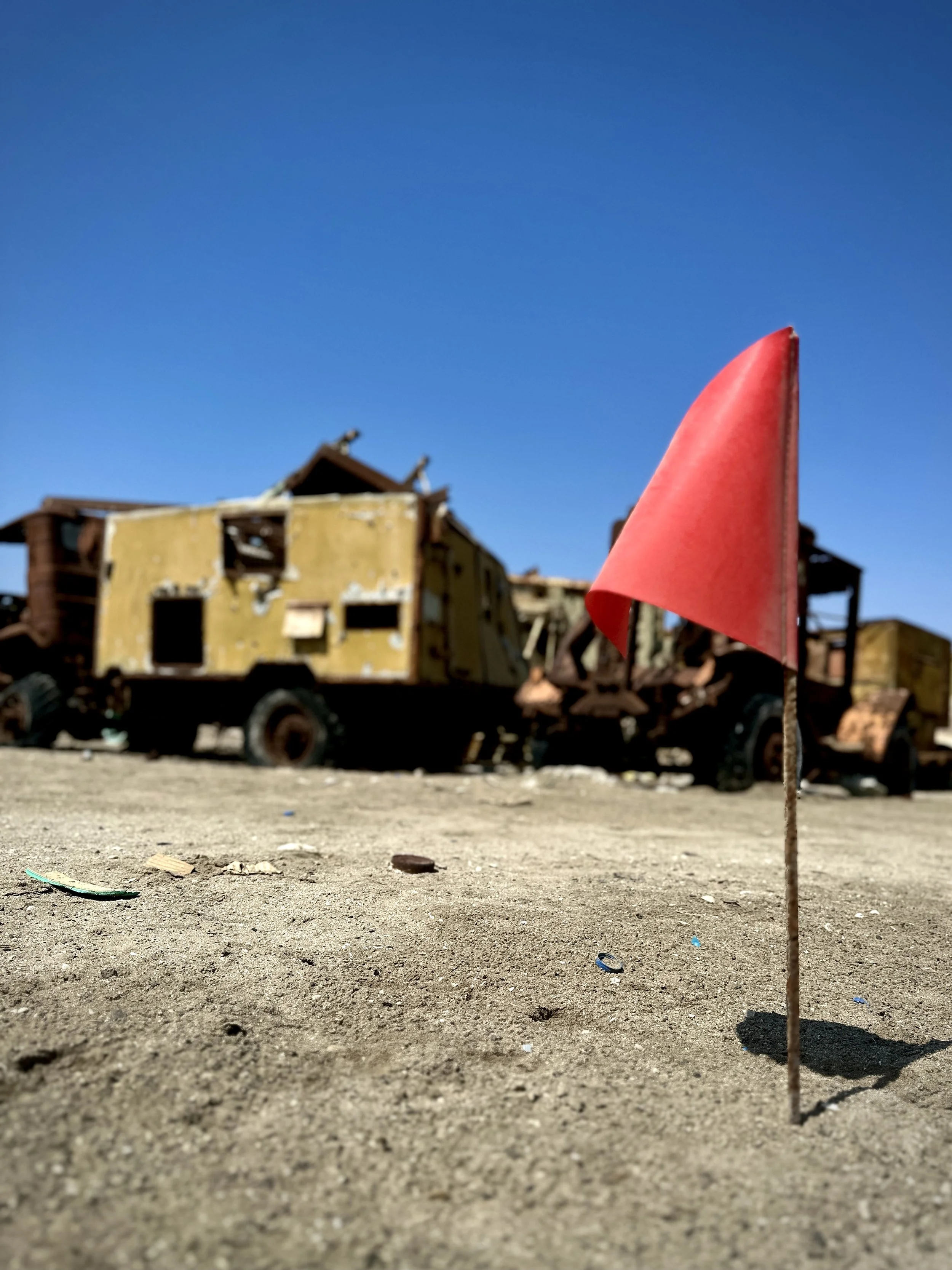 A red marker flag identifies a hazardous or controlled search area during clearance work at Aden International Airport. Such markers help teams map progress and warn others away from potentially contaminated ground.